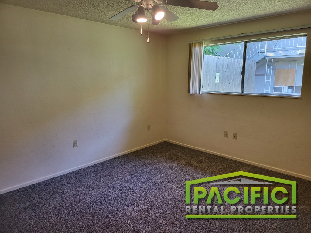an empty living room with a ceiling fan and a window