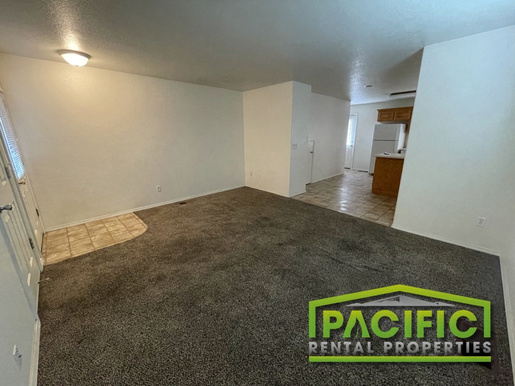 an empty living room with a carpeted floor and an empty kitchen