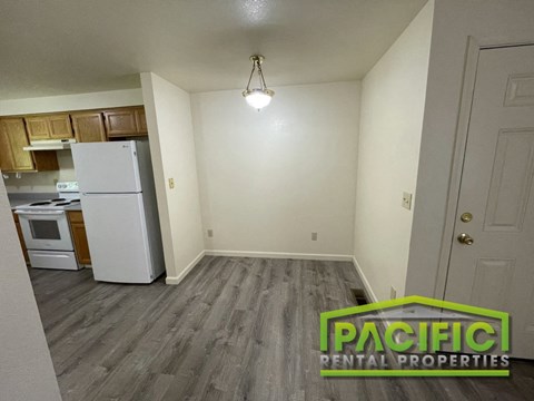 an empty living room with a kitchen with a refrigerator and