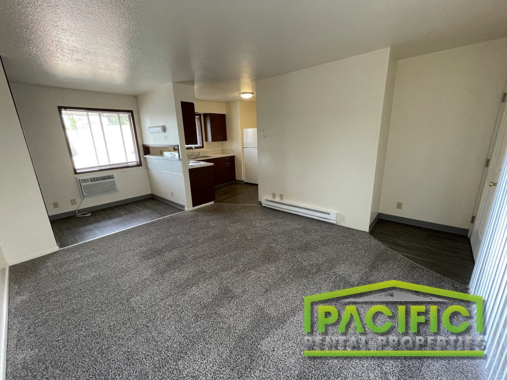 an empty living room with gray carpet and a kitchen