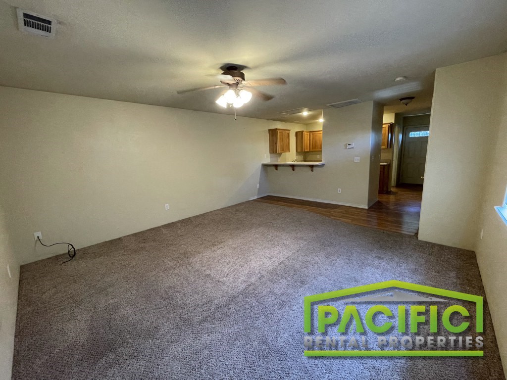 an empty living room with a ceiling fan and a carpeted floor