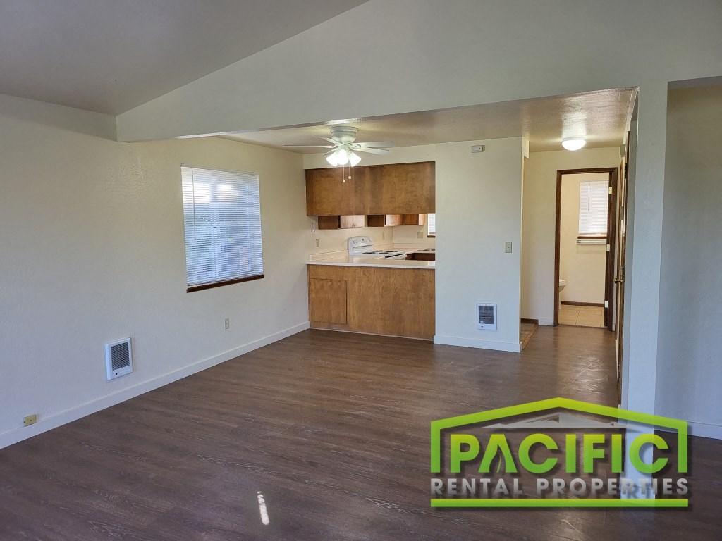 an empty living room and kitchen with wood flooring and a ceiling fan