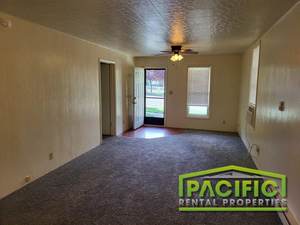 an empty living room with a ceiling fan and a door to a yard