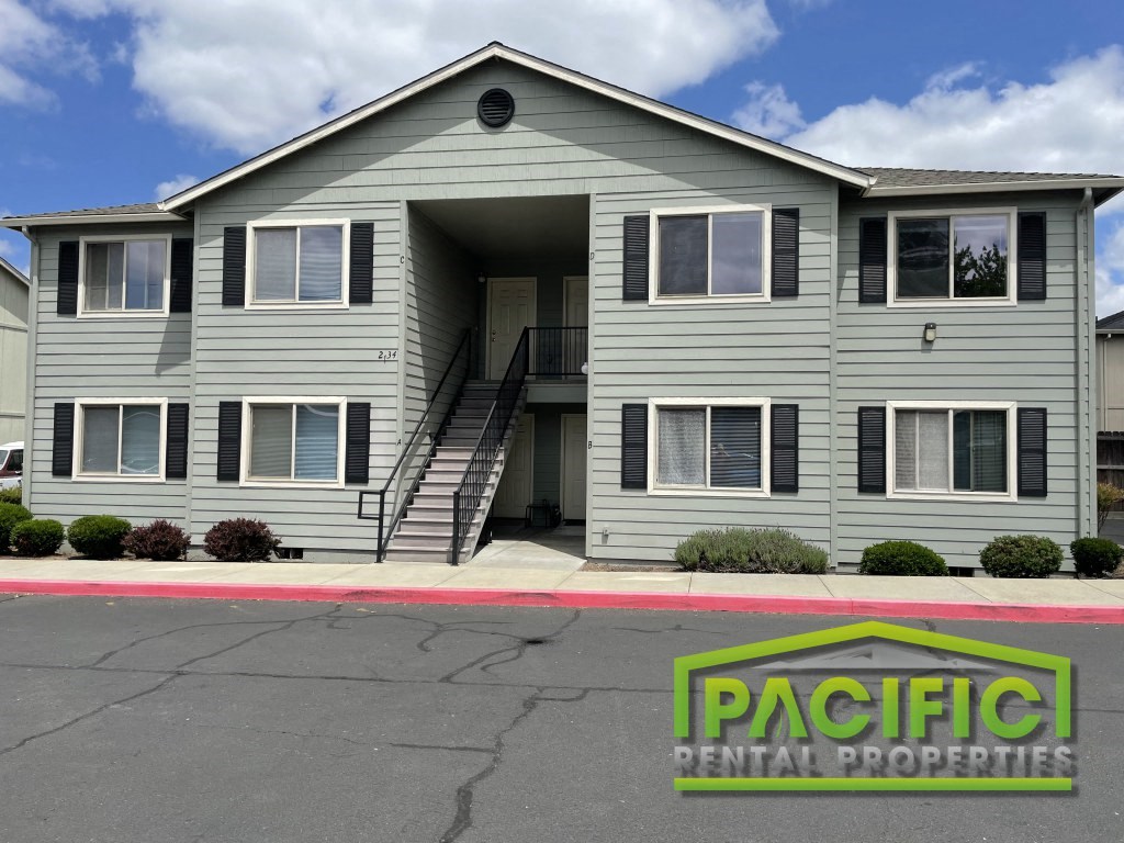 a grey apartment building with a pacific rental properties sign in front