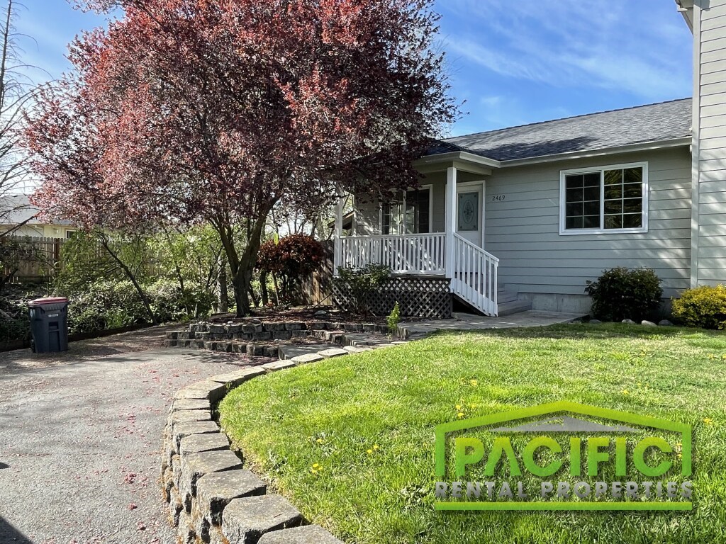 A house with a driveway and a tree with pink leaves.
