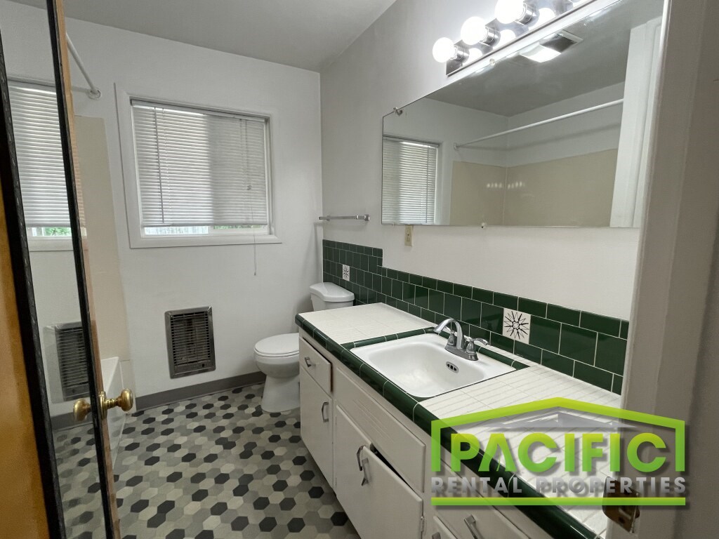 A bathroom with a green tile backsplash and a white toilet.