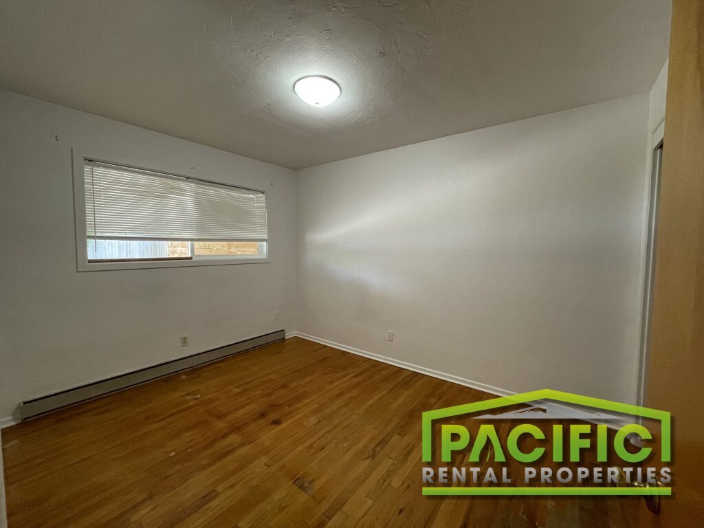 A room with wooden flooring and a window with blinds.