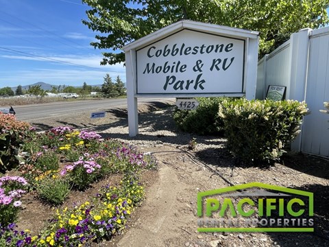 A sign for Cobblestone Mobile & RV Park with a garden in the foreground.