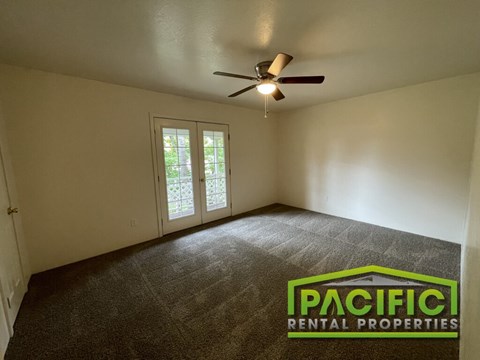 A room with a carpet floor, a ceiling fan, and a door leading outside.