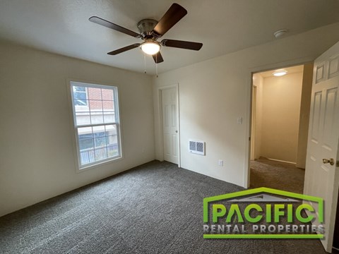 A room with a ceiling fan and a window with a view of a balcony.