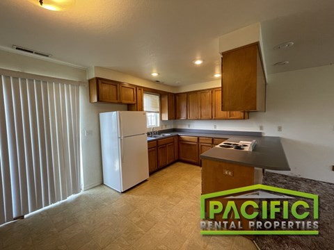 A kitchen with a refrigerator, cabinets, and a countertop is shown in an empty apartment.