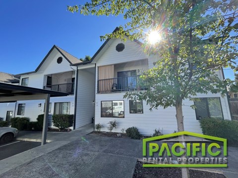 A sunny day at a Pacific Rental Properties property with a white house and a tree in the foreground.