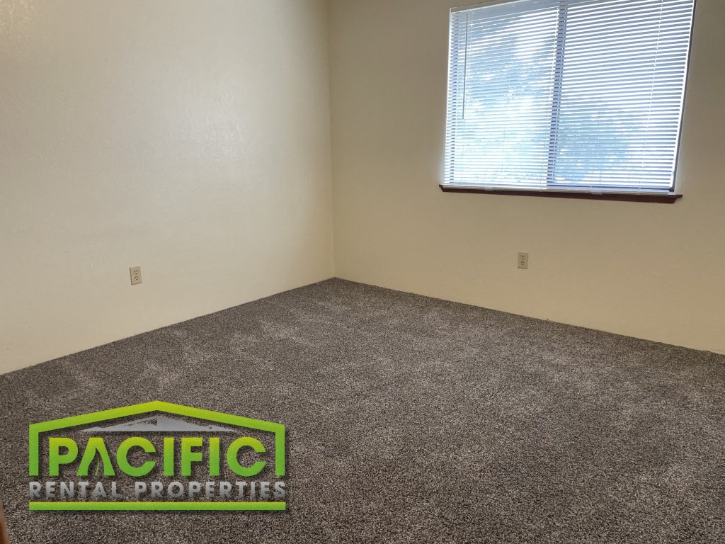 a carpeted room with a window and pacific rental properties logo on the floor