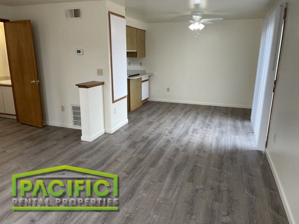 an empty living room with wood flooring and a kitchen
