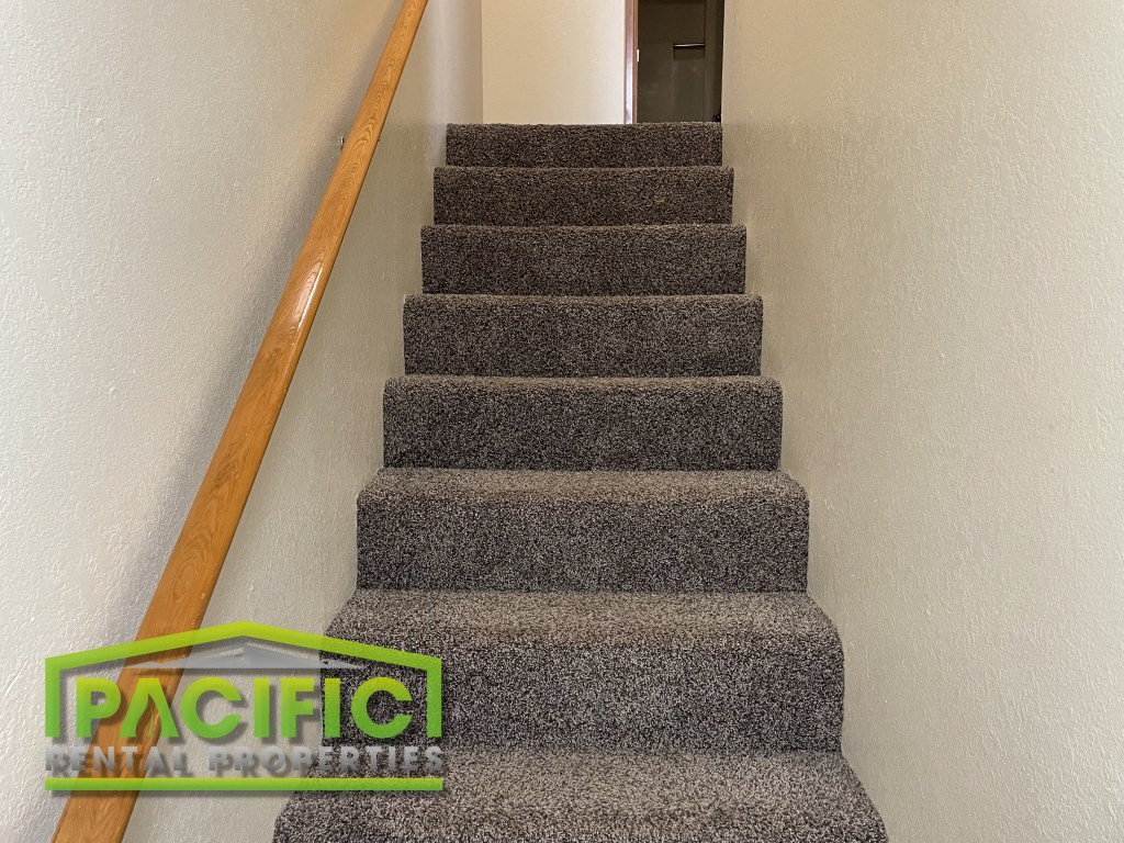a carpeted staircase with a wooden rail and gray carpet on the stairs