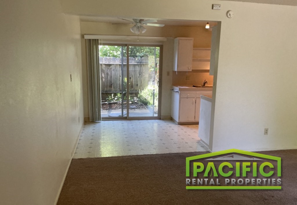 an empty living room with a kitchen and a sliding glass door