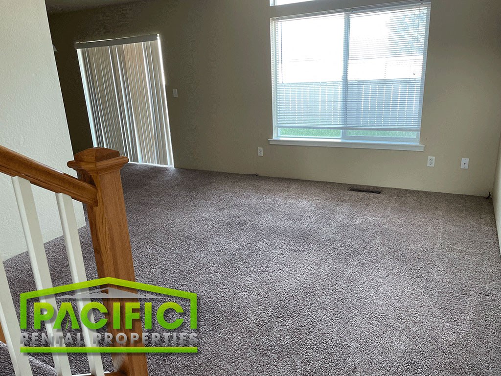 a carpeted living room with a staircase and a window
