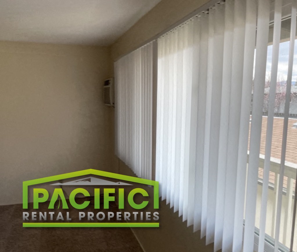 a window with white blinds and a pacific rental properties sign on the floor