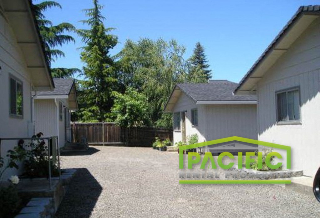 a driveway in front of a white house and a backyard with trees