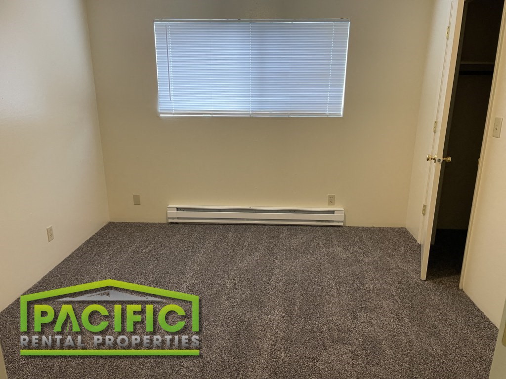 a carpeted room with a window and pacific rental properties logo on the floor