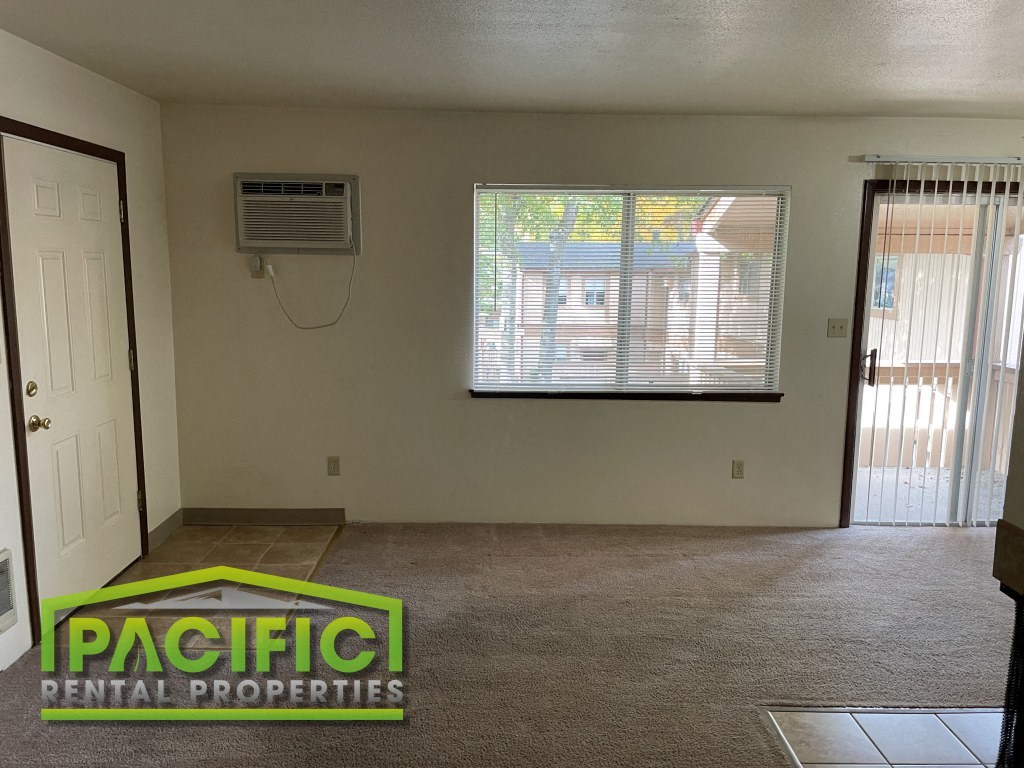 an empty living room with an air conditioner and a window