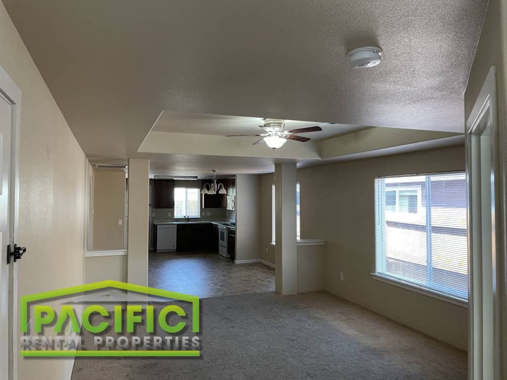 an empty living room with a ceiling fan and a kitchen
