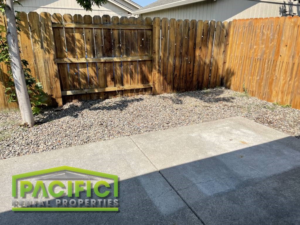 a yard with a wooden fence and a sidewalk in front of a house