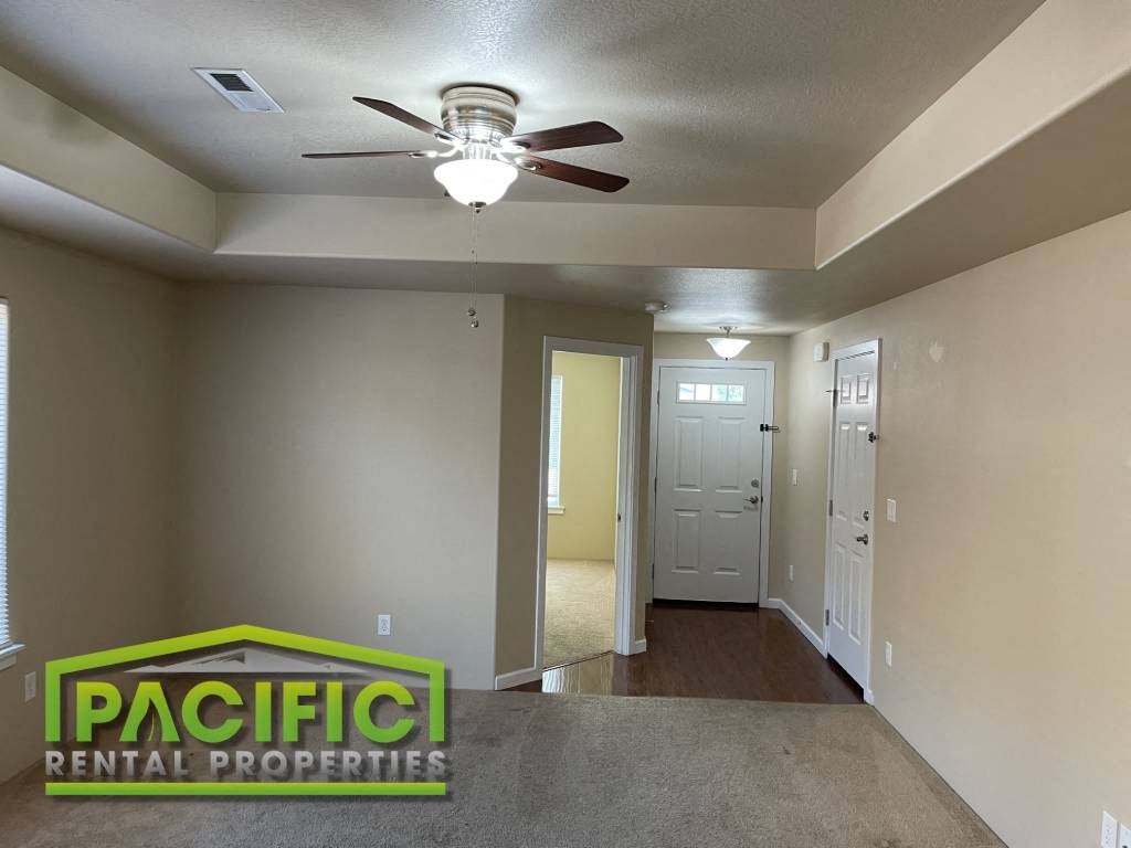 an empty living room with a ceiling fan and a door to a hallway