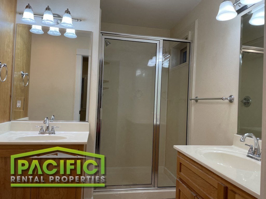 a bathroom with a shower and two sinks and a pacific rental properties logo
