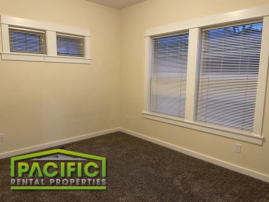 a bedroom with two windows and a carpet and pacific rental properties logo on the