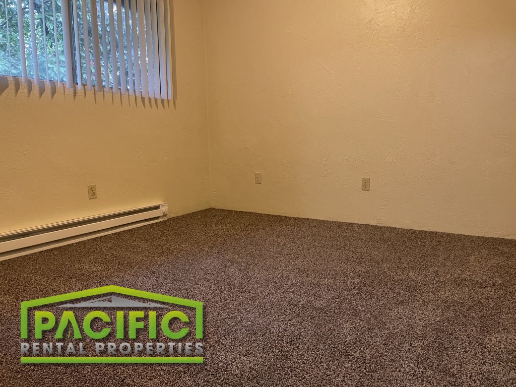 a carpeted room with a window and pacific rental properties logo on the floor