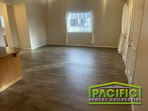 A spacious room with wooden flooring and a window with white curtains.