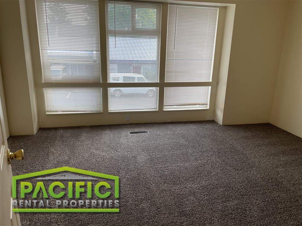 a carpeted room with a window and pacific rental properties logo on the floor