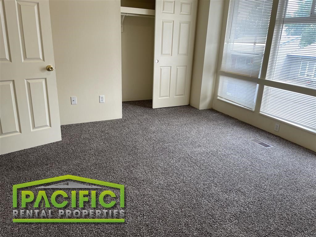 a carpeted living room with a door and a pacific rental property logo on