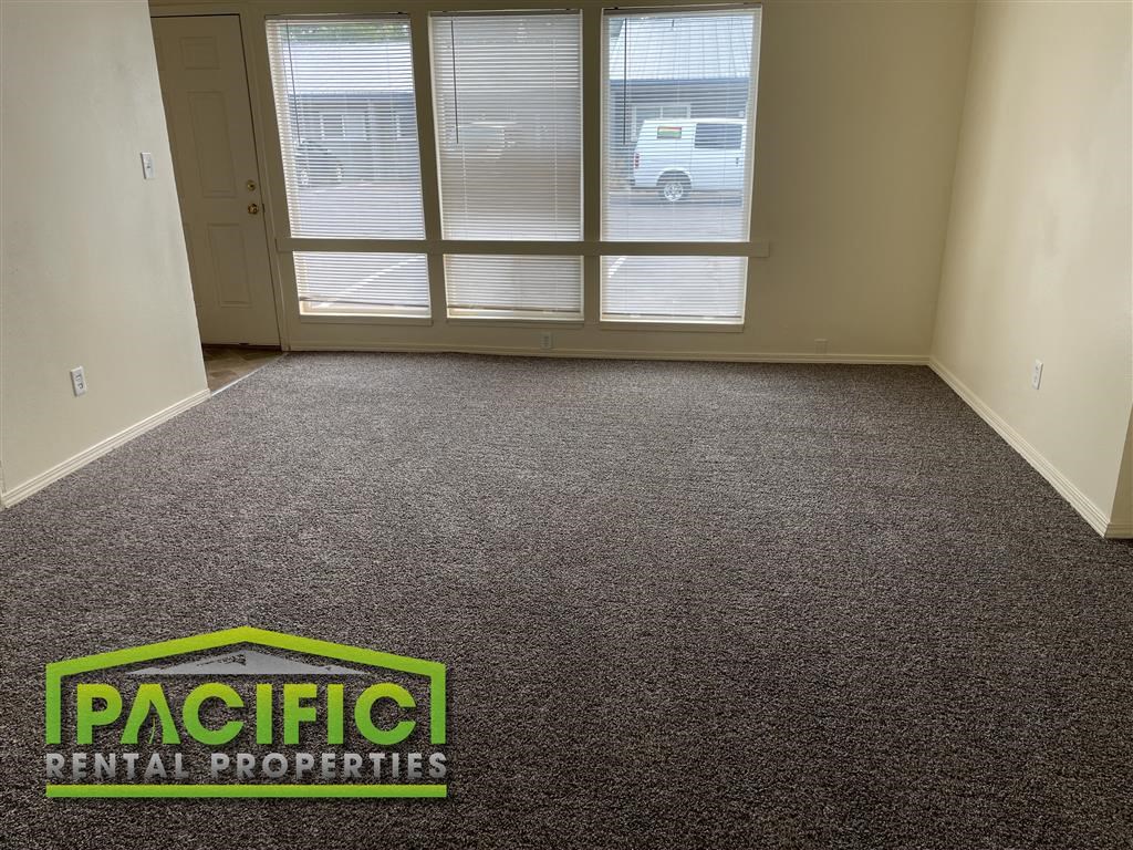 a carpeted room with a pacific rental properties logo on the floor