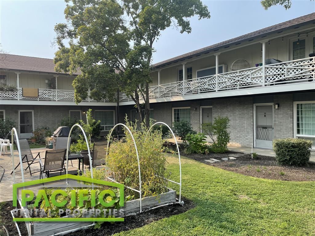 a patio in front of a building with a porch and a garden