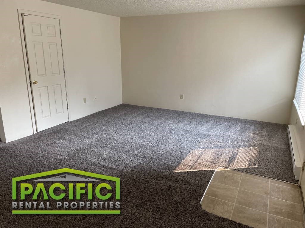 an empty room with carpet and a door    pacific rental properties logo