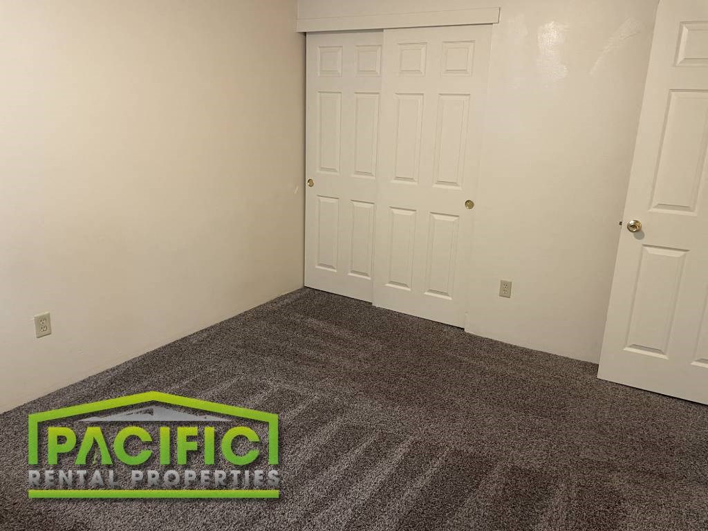 a carpeted room with a door and a pacific rental properties logo