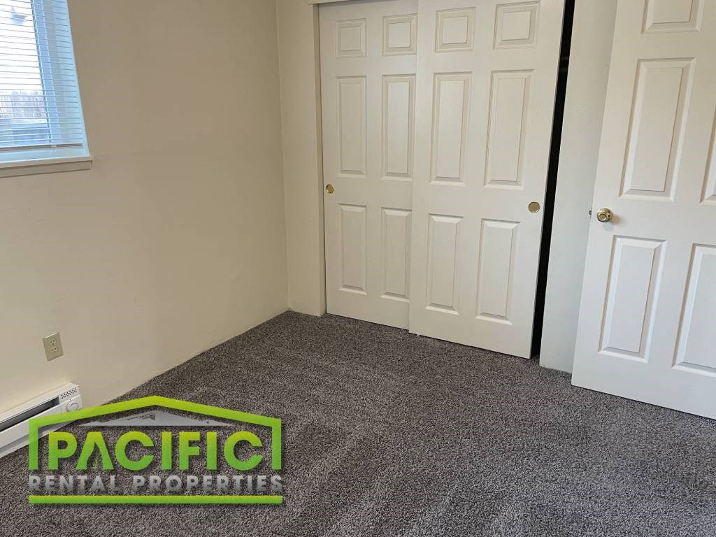 a carpeted room with a door and a pacific rental properties logo