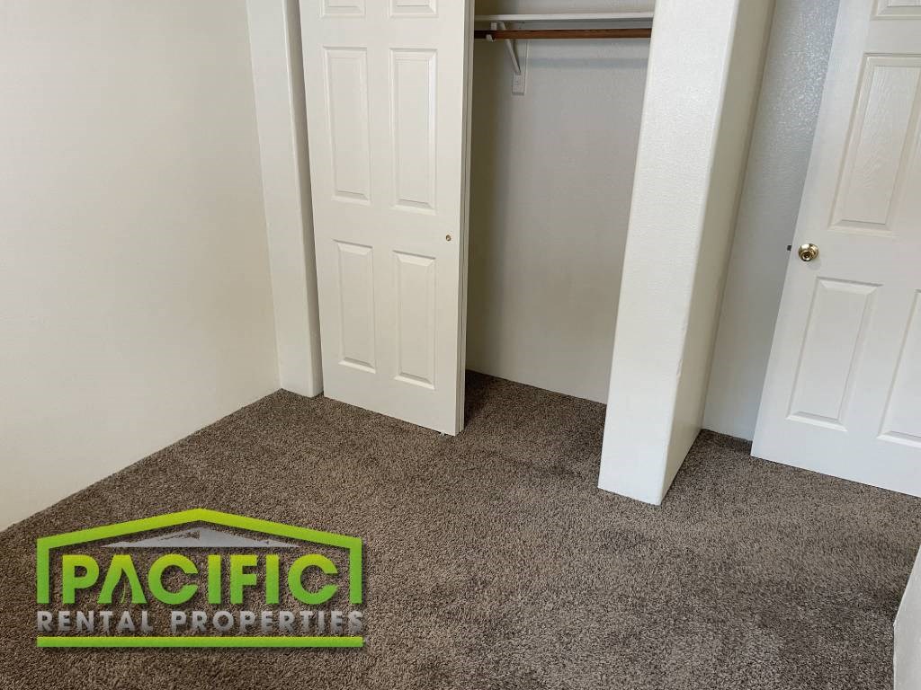 a carpeted room with a closet and a pacific rental properties logo on the