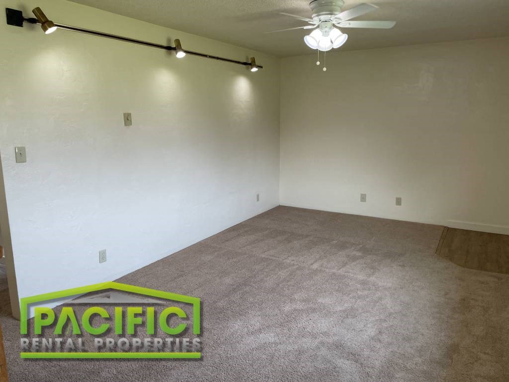 an empty living room with a carpeted floor and a ceiling fan