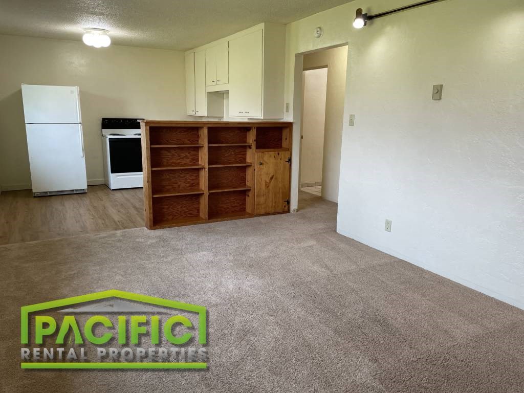 an empty living room with a refrigerator and a book shelf