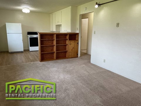 an empty living room with a refrigerator and a book shelf