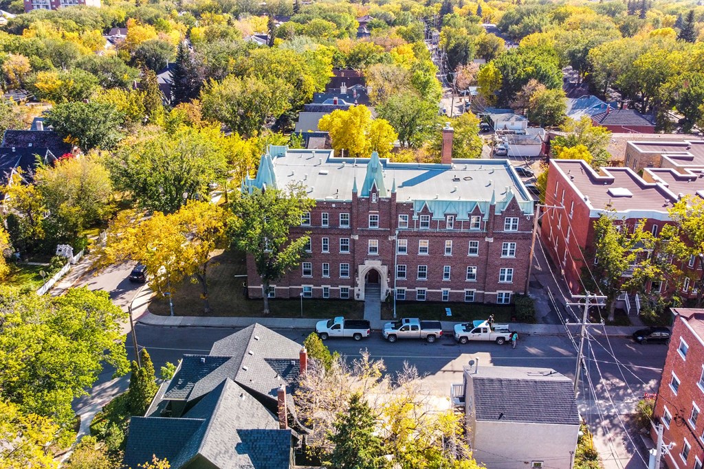 A large red brick building with a green roof sits in the middle of a parking lot.