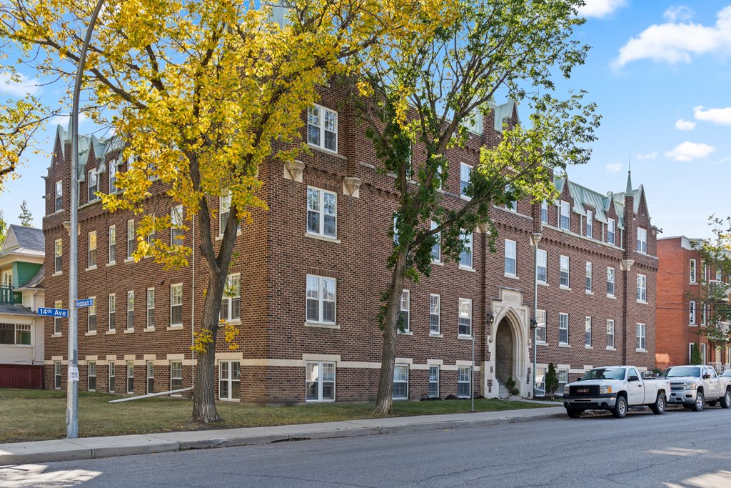 A large red brick building with a green roof and a tree with yellow leaves in front.