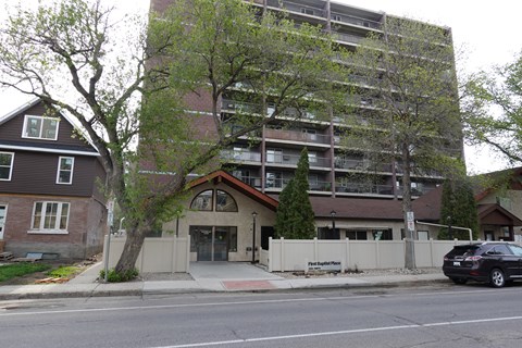 A black car is parked on the side of the road in front of a building.