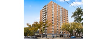 A tall apartment building with a parking lot in front.