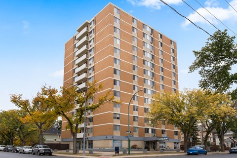 A tall apartment building with a parking lot in front.