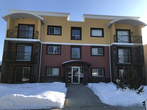 A multi-story apartment building with balconies and snow on the ground.