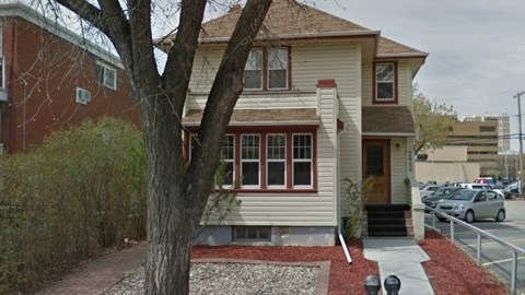 A house with a red brick wall and a tree in front.